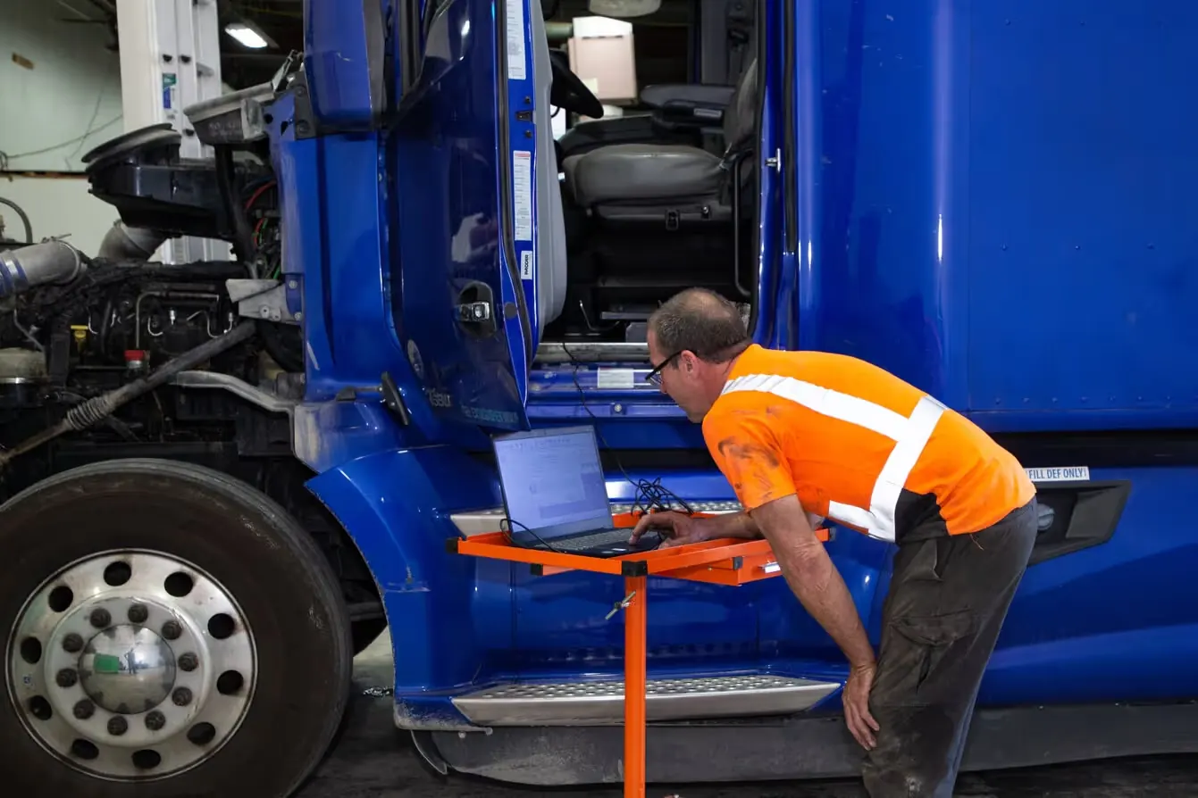 Technician running diagnostics on a blue semi truck