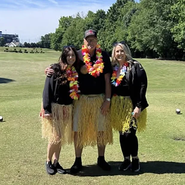Three team members in leis and grass skirts at a golf outing